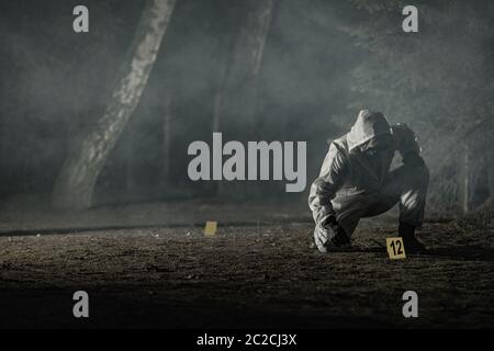 Ricerca di tracce e prove di crimine marcatori collocando da Forensic Officer in Hazmat Suit e Guanti. Foresta di Foggy scuro. Concetto di tema scena del crimine. Foto Stock