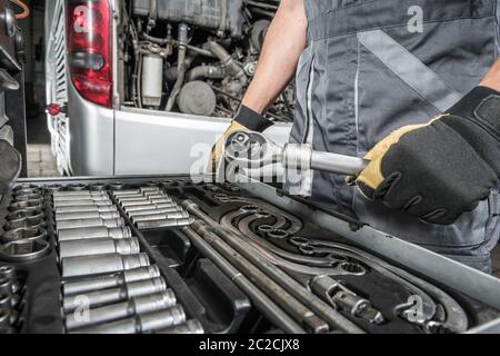 Tecnico di servizio del bus del pullman che sceglie gli attrezzi giusti per il lavoro. Tecnico di autobus caucasico e il set di attrezzi. Tema industria dei trasporti. Foto Stock