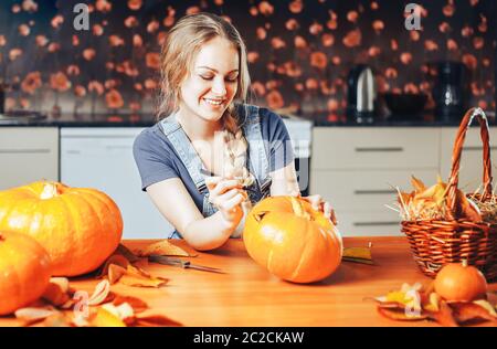 una bella donna bionda dipinge zucche per halloween a casa in cucina Foto Stock