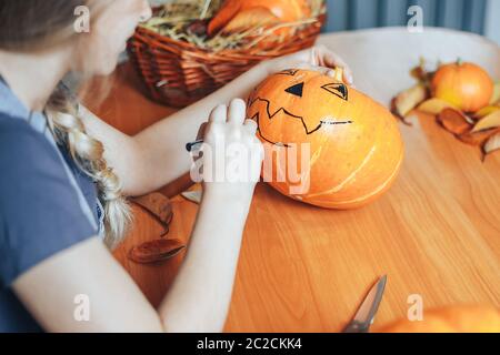 una bella donna bionda dipinge zucche per halloween a casa in cucina Foto Stock