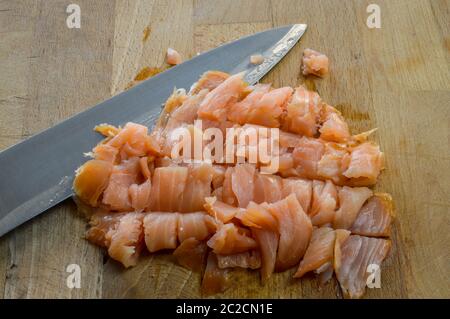 Salmone affumicato fresco tritato su un tagliere di legno con un coltello da cucina primo piano. Foto Stock
