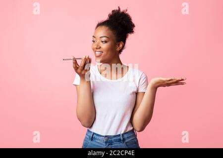 Felice addetta afro che usa l'assistente vocale sullo smartphone Foto Stock