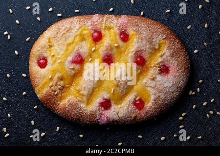 Vista ad alto angolo di una coca de Sant Joan, una tipica dolce torta piatta della Catalogna, Spagna, mangiata a San Giovanni, su una superficie di tessuto nero spruzzata Foto Stock