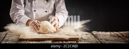 Esplosione di farina sospesa in aria in una pizzeria cucina come lo chef prepara una porzione di impasto per la crosta in un panorama rustico banner con c Foto Stock