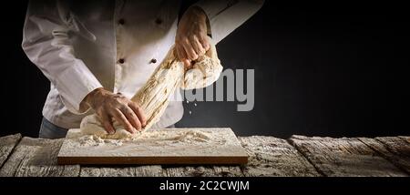 Baker chef o di estensione di una porzione di pasta cruda come egli lavora su di esso durante la preparazione per la cottura in un panorama rustico banner con spazio di copia Foto Stock