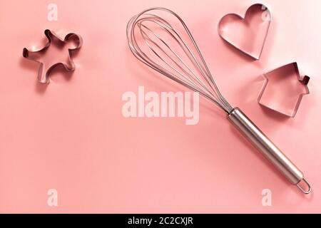 La frusta in acciaio ospita l'uomo e la taglierina a forma di cuore sulla destra dall'alto. Vista dall'alto in piano. Concetto di cucina dolciaria con spazio di copia su rosa brillante Foto Stock