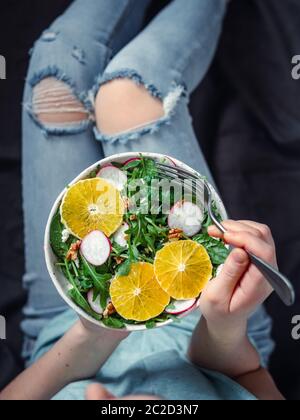 Donna in jeans a letto, tenendo in mano piatto di insalata vegana Foto Stock