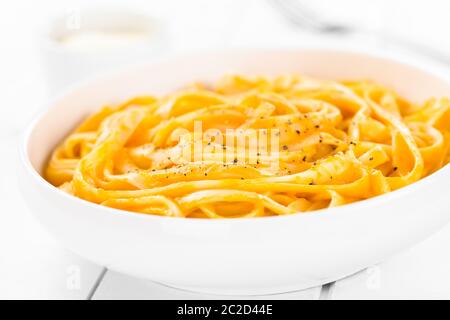 Fettuccine con freschi fatti in casa di zucca cremosa salsa Alfredo guarnita con pepe nero macinato fresco e servito in tazza, formaggio grattugiato e per Foto Stock