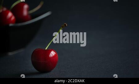 Primo piano vista della frutta fresca dolce ciliegia matura in luce scura e sfondo nero con gocce d'acqua basso chiave ancora vita Foto Stock