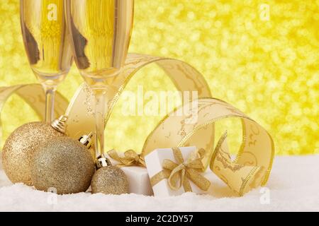 Due wineglass con champagne, scatole regalo e decorazioni natalizie su una superficie innevata su sfondo dorato festoso. Natale e Capodanno g Foto Stock