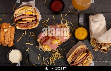 Fast food e concetto di alimentazione malsana in stile venezuelano. Hamburger, hot dog, bastoncini fritti e salse su sfondo nero. Menu menu snack bar Foto Stock