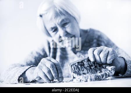 In questione anziani 96 anni vecchia donna seduta a tavola in casa e il conteggio delle monete rimanenti dai regimi pensionistici nel suo portafoglio dopo il pagamento di fatture. Unsustainabi Foto Stock