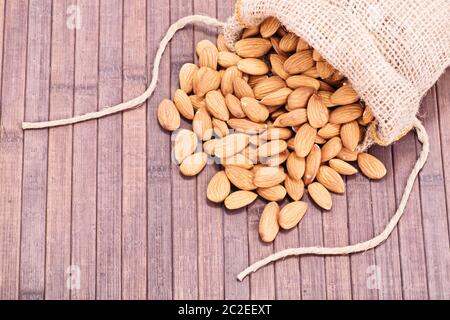 Immagine ravvicinata di mandorle fuoriuscito versato da un sacco di tela, su uno sfondo di legno. Foto Stock