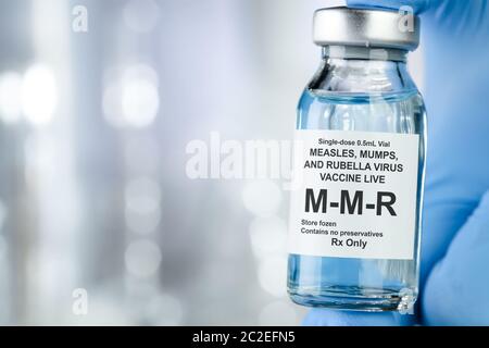 Il concetto di assistenza sanitaria con una mano in blu guanti medicali azienda MMR, morbillo, parotite e rosolia, flaconcino di vaccino Foto Stock