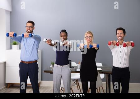 Felice giovani imprenditori in piedi in fila esercizio con manubri in Office Foto Stock