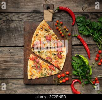 Cotto al forno per pizza tonda con salsicce affumicate, funghi, pomodori, formaggi e aneto, cibo affettato su un di legno marrone, scheda close up Foto Stock