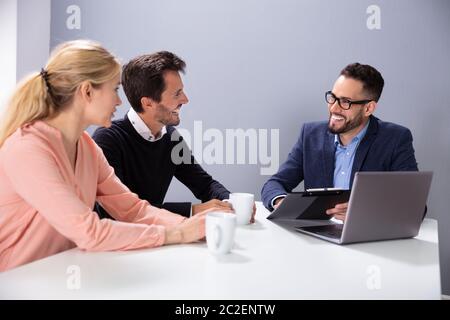 Felice Coppia Giovane consultazione amichevole maschio Advisor finanziario con tazze da caffè alla scrivania in ufficio Foto Stock