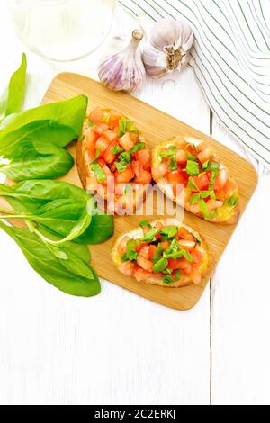 Bruschetta con pomodoro, basilico e spinaci su una piastra, fresche foglie di spinaci, igienico e olio vegetale in un decanter contro luce pannello di legno da abo Foto Stock