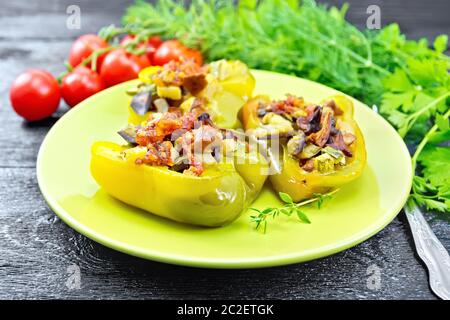 Peperoni ripieni con funghi, pomodori, zucchine, melanzane e cipolle, condito con vino, aglio, timo e spezie in una piastra verde su legno Foto Stock