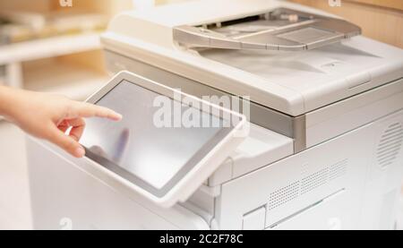 Mano femminile premendo il monitor touchscreen della copiatrice per copiare un documento cartaceo, uno scanner nella copiatrice e il nuovo laser tec Foto Stock