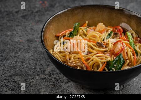 Mescolare le tagliatelle fritte con verdure e gamberetti in una ciotola nera. Sfondo ardesia. Vista dall'alto. Foto Stock