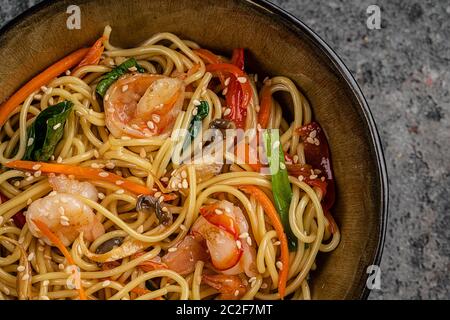 Mescolare le tagliatelle fritte con verdure e gamberetti in una ciotola nera. Sfondo ardesia. Vista dall'alto. Foto Stock