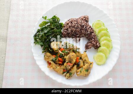 Mescolare il pesce fritto con peperoncino e basilico, servito con riso al vapore e cetrioli, piatto caldo e piccante. Foto Stock