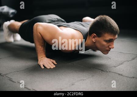 Ritratto di colpo centrale di forte muscolare che fa esercizio di spinta-up sul pavimento Foto Stock