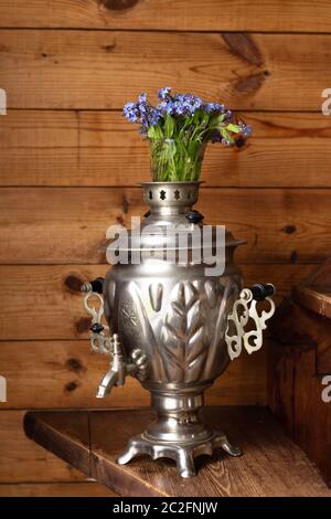 Samovar in metallo antico e bouquet di fiori blu su sfondo di legno Foto Stock