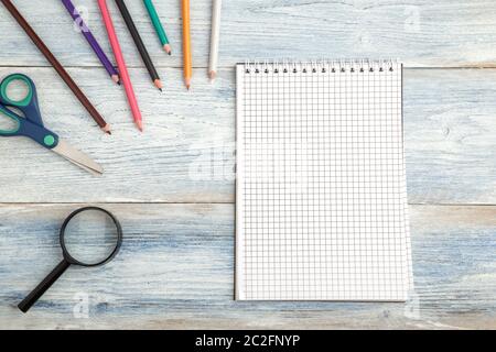 Articoli di cancelleria, un notebook di carta e di una lente di ingrandimento su una luce blu in legno vecchio sfondo. vista superiore. laici piatta Foto Stock