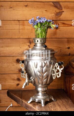 Samovar in metallo antico e bouquet di fiori blu su sfondo di legno Foto Stock