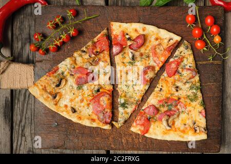 Pizza cotta al forno con salsicce affumicate, funghi, pomodori, formaggi e aneto, cibo affettato su un di legno marrone, scheda close up Foto Stock