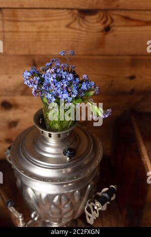 Samovar in metallo antico e bouquet di fiori blu su sfondo di legno Foto Stock