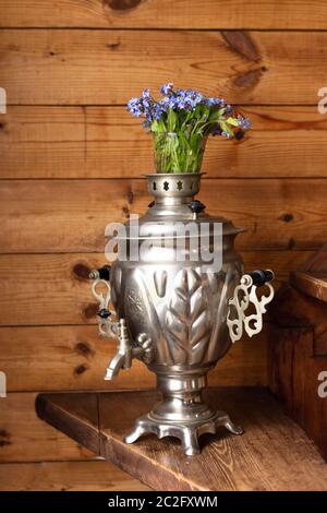 Samovar in metallo antico e bouquet di fiori blu su sfondo di legno Foto Stock