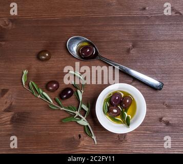 Olio di oliva e di olive su una superficie in legno con alcuni rami di olivo Foto Stock