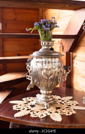 Samovar in metallo antico e bouquet di fiori blu su sfondo di legno Foto Stock