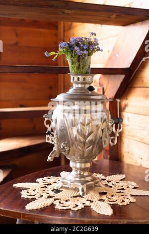 Samovar in metallo antico e bouquet di fiori blu su sfondo di legno Foto Stock