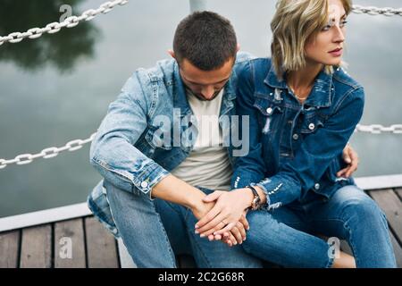 Bella coppia alla moda che posa sul ponte di fiume indossando jeans denim Foto Stock