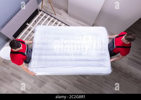 Due maschio Professional Movers In Uniforme mettendo il materasso sul letto in casa nuova Foto Stock