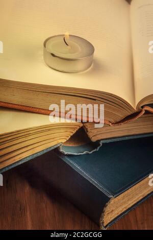 Lettura al buio a lume di candela. Una pila di vecchi libri con una candela bruciante e un posto per il testo, fuoco selettivo, imag tonato Foto Stock