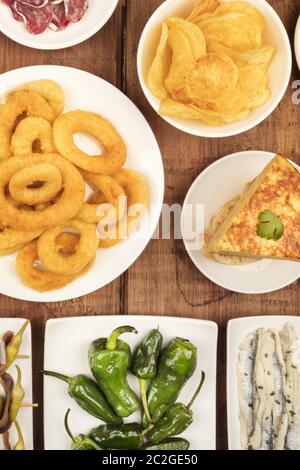 Tapas spagnole, una varietà di snack. Anelli di totano, tortilla, sardine, padron peperoni, Top Shot al buio su un rustico sfondo di legno Foto Stock