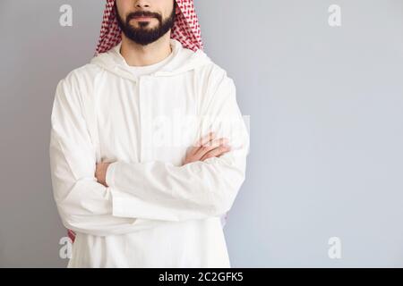 Uomo arabo sicuro senza volto ha attraversato le braccia su uno sfondo grigio Foto Stock