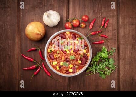 Chili con carne, uno stufato messicano con fagioli rossi, carne e peperoncini, sparato dall'alto su uno sfondo di legno rustico scuro wi Foto Stock