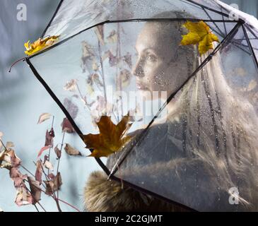 Donna sotto un ombrello trasparente con foglie di autunno Foto Stock