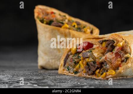 Burritos e shawarma avvolge con verdure di manzo e maiale su tavola di legno su fondo nero Foto Stock