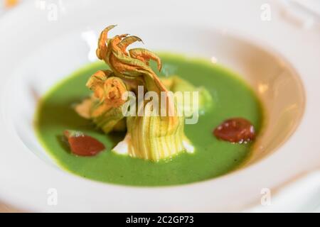 Piatto di zuppa di zucchine con fiori di zucca e pomodorini decorazione. Servita per matrimonio o evento. Foto Stock