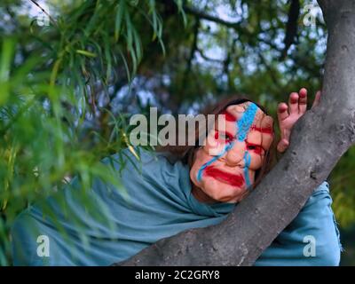 Una forma dissimulata di persona con un inquietante maschera di Halloween si affaccia tra i rami di un albero. Foto Stock