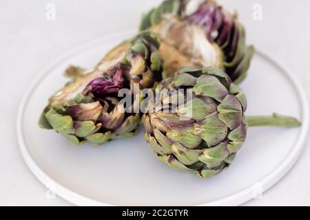 Immagine minimalista dei carciofi in una piastra di ceramica bianca. Composizione orizzontale. Foto Stock
