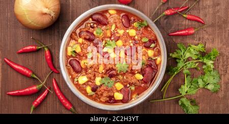 Un panorama di chili con carne, girato dalla parte superiore al buio su un rustico sfondo di legno con ingredienti Foto Stock