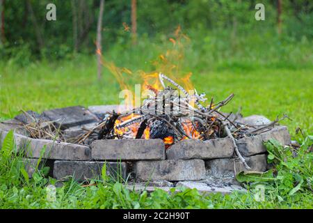 Refrattario fuoco campfire in mattoni a fuoco e erba verde falò offuscata sullo sfondo Foto Stock